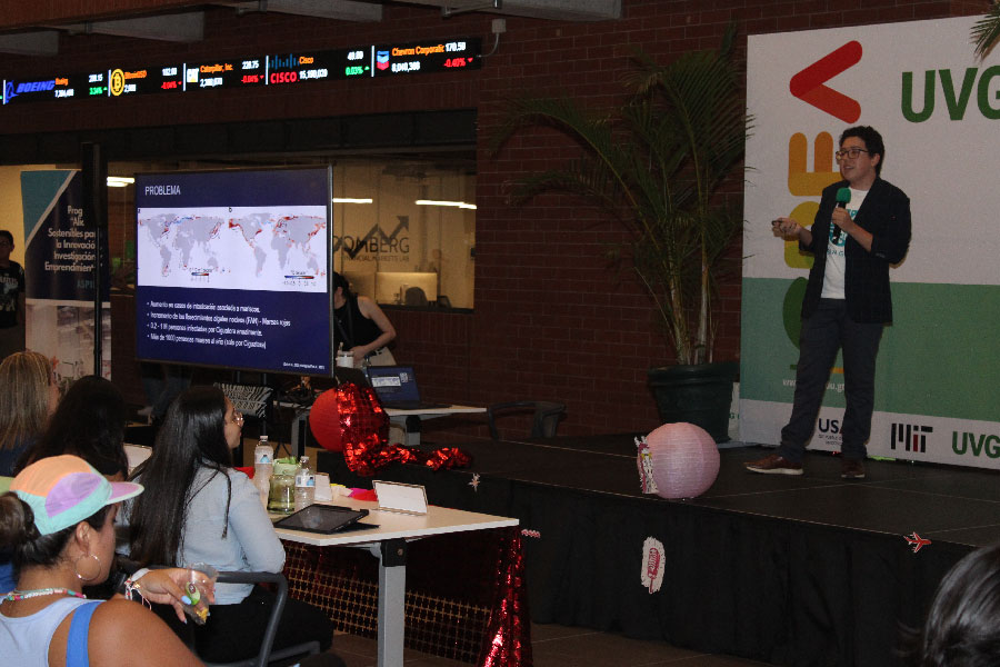Hombre parado en escenario hablando con micrófono. 