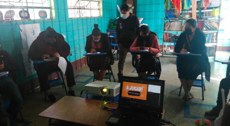 Una foto de cinco personas adultas sentadas en escritorios en una sala; están trabajando en leer o llenar material impreso.