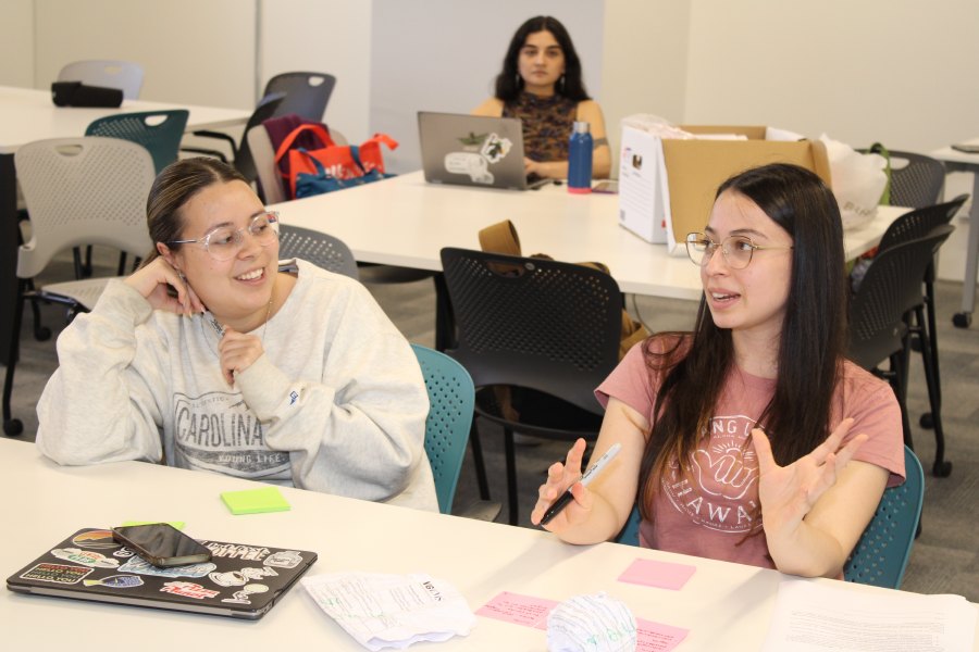 Two women talking at a table with post it notes being used and a closed laptop.
