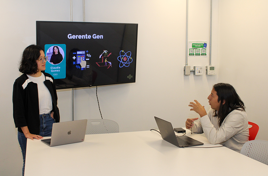 Two people with laptops in a conference room talking in front of a screen with their presentation.