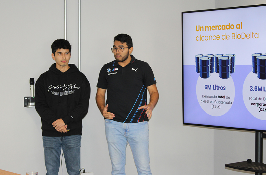 Two men in front of room presenting from a large screen.