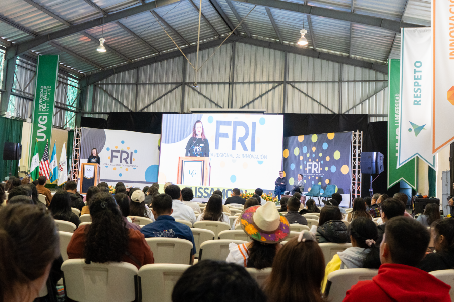 A group of people sitting while paying attention to a woman on stage.