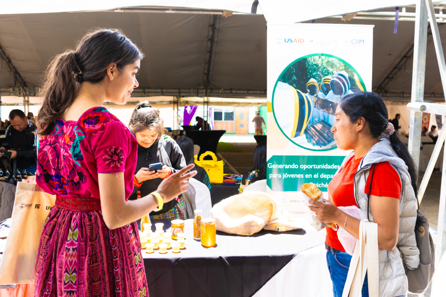 Two women speaking in front of a table with honey jars.