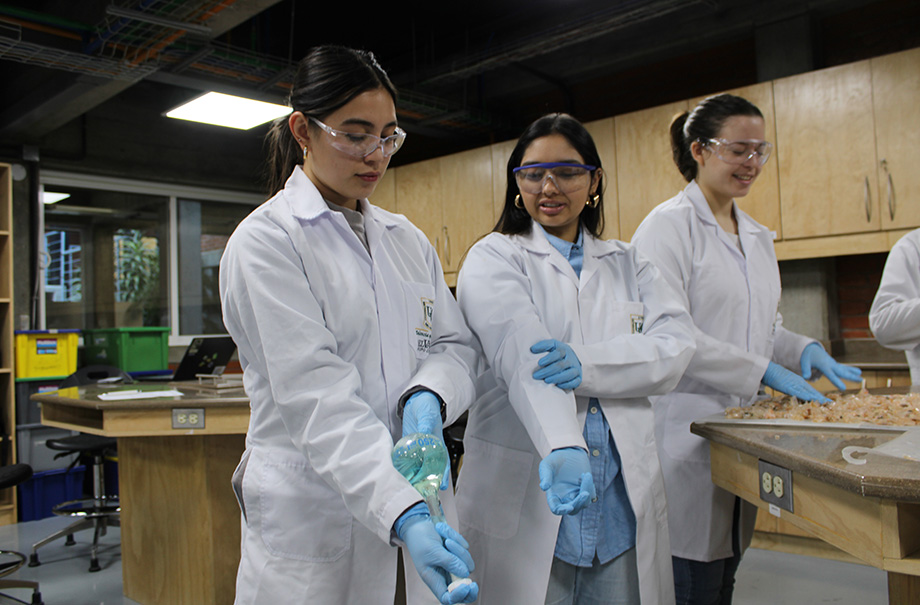 two women in lab coats training on using a flask to mix liquids