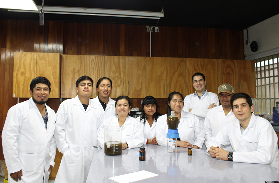 Ocho personas de las cooperativas agrícolas Ija'tz e Innoc posan en el laboratorio de extracción de aceites esenciales de la Universidad del Valle de Guatemala. Rodrigo Aragón está al extremo derecho y Elizabeth es la cuarta desde la izquierda.