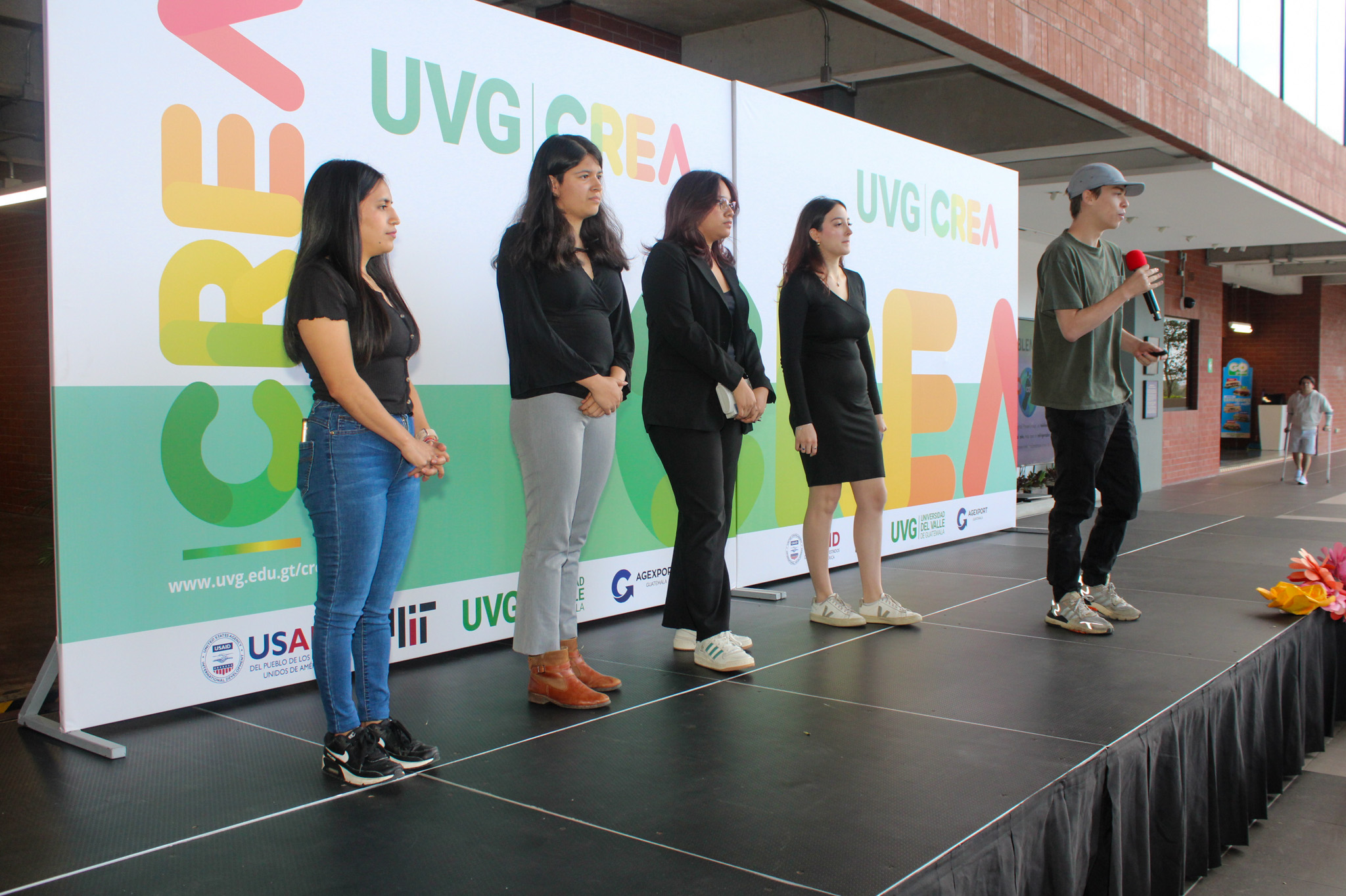 Cinco personas paradas, una de ellas está sosteniendo un prototipo y otra un micrófono. 