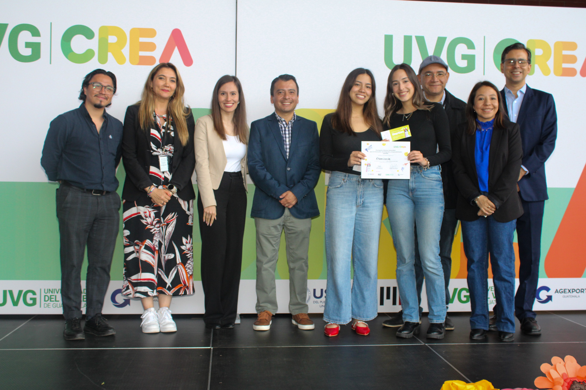 Nueve personas paradas y dos mujeres sosteniendo un reconocimiento.